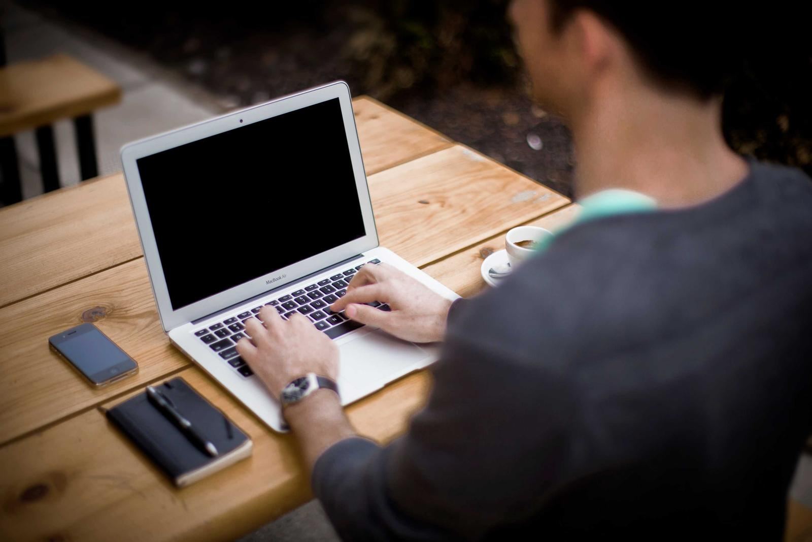 A developer typing on a laptop at a wooden table